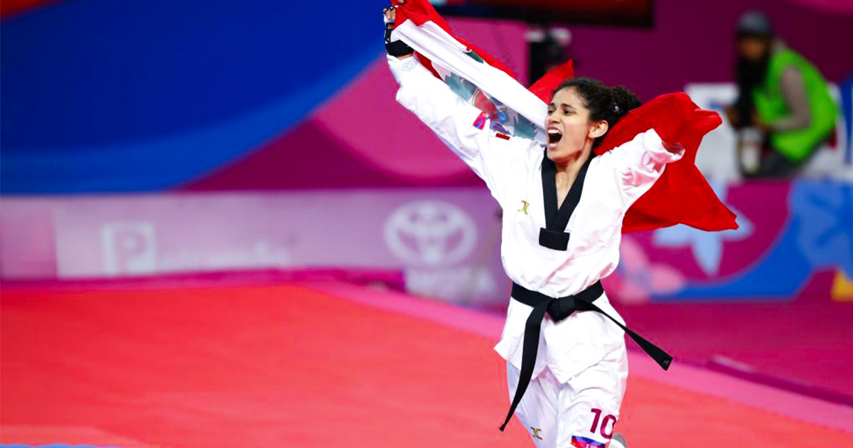 Angélica Espinoza, celebra su medalla de oro corriendo y gritando sosteniendo la bandera del Perú en lo alto con los brazos abiertos.   