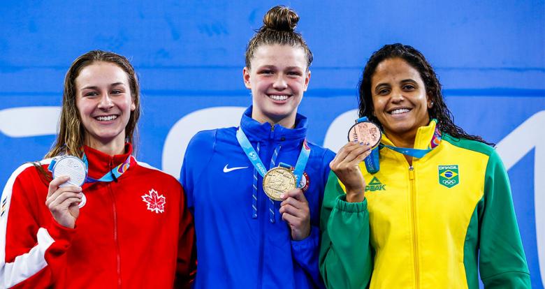 Swimmers Alexia Zevnik from Canada (silver), Margo Greer from the United States (gold) and Larissa Martins de Oliveira from Brazil (bronze) show their medals after competing in women’s 100 m freestyle at the National Sports Village – VIDENA