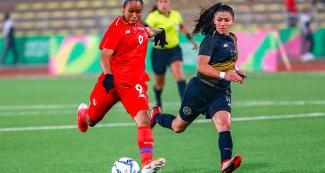 Panamanian Karla Riley about to kick the ball while Costa Rican María Bermúdez watches attentively