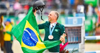 Brazilian Carlos Parro celebrates third place in Lima 2019 equestrian event with his medal and national flag at the Army Equestrian School