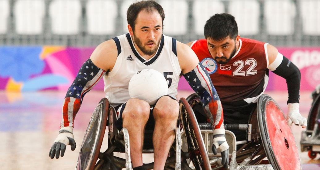 Charles Aoki (USA) sosteniendo el balón entre sus piernas mientras le lleva la delantera a un jugador chileno en partido de rugby en silla de ruedas en los Parapanamericanos Lima 2019. 